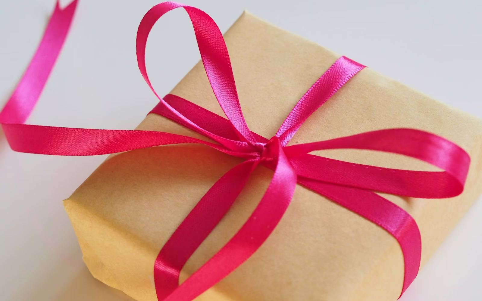 Kotak hadiah berbungkus kertas cokelat dengan pita merah muda