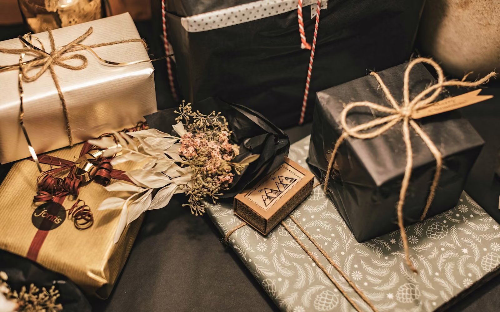 Beberapa kotak hadiah berbungkus kertas emas dan hitam dengan tali rami