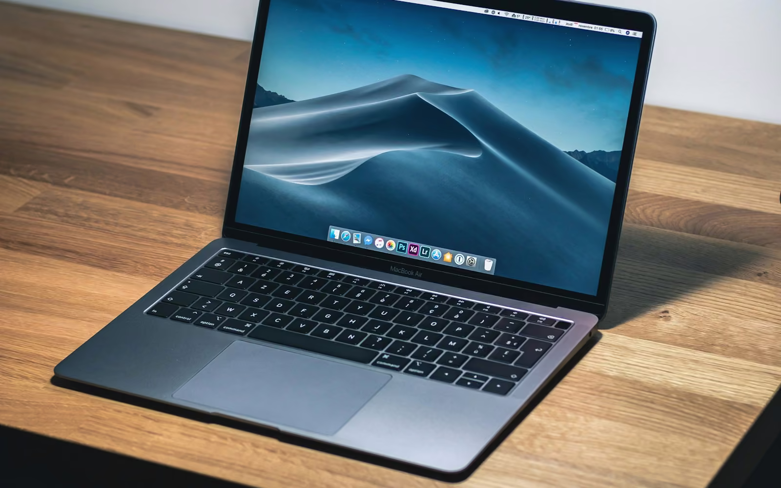 Laptop terbuka di atas meja kayu dengan layar bergambar pegunungan