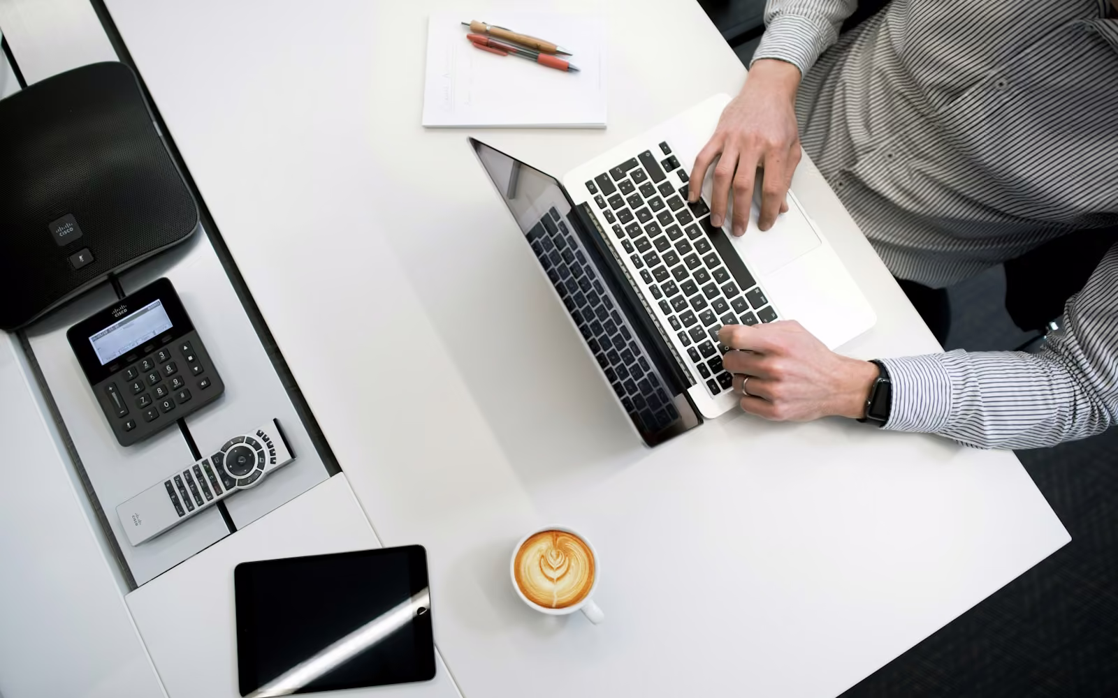 Meja kerja putih dilihat dari atas dengan laptop, tablet, dan secangkir kopi