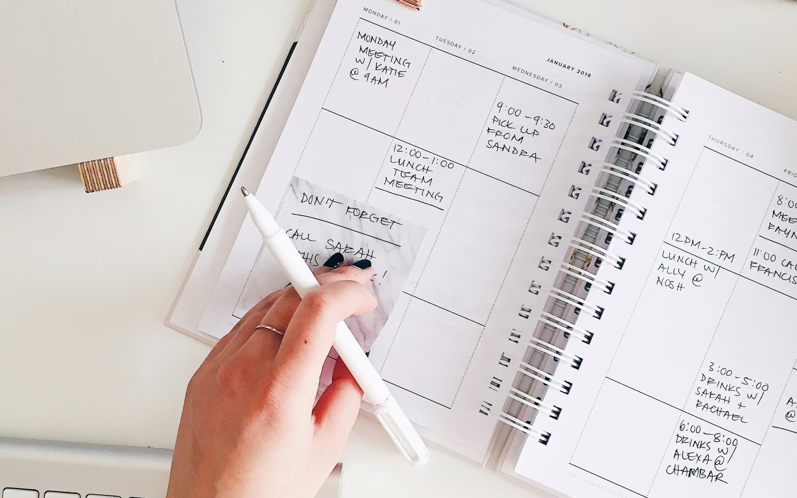 Tangan menulis di buku agenda mingguan di samping keyboard