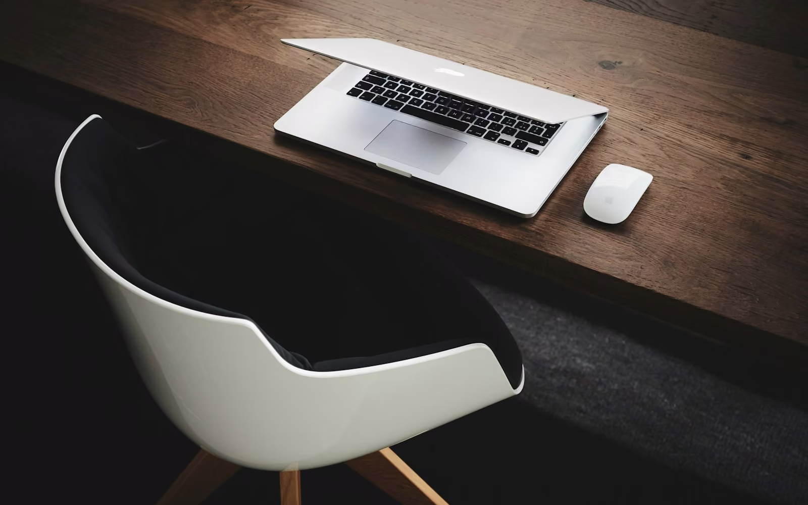 Laptop di meja kayu gelap dengan kursi putih