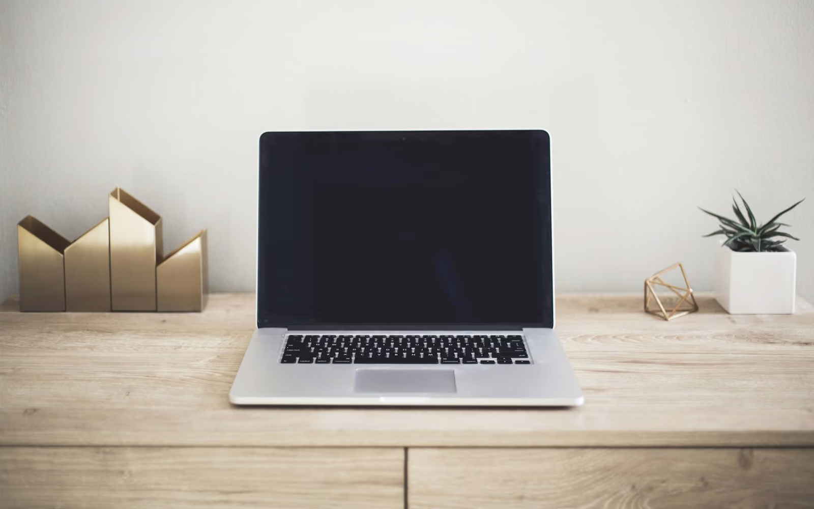 Laptop di atas meja kayu terang dengan hiasan sederhana