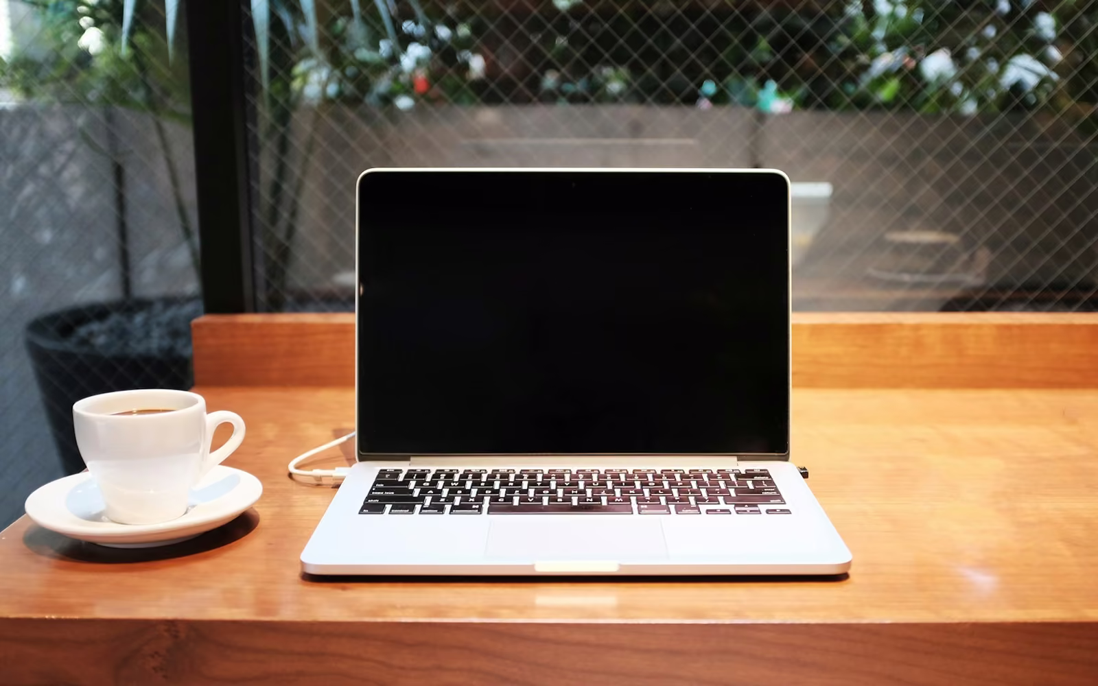 Laptop terbuka di samping cangkir kopi di meja kayu